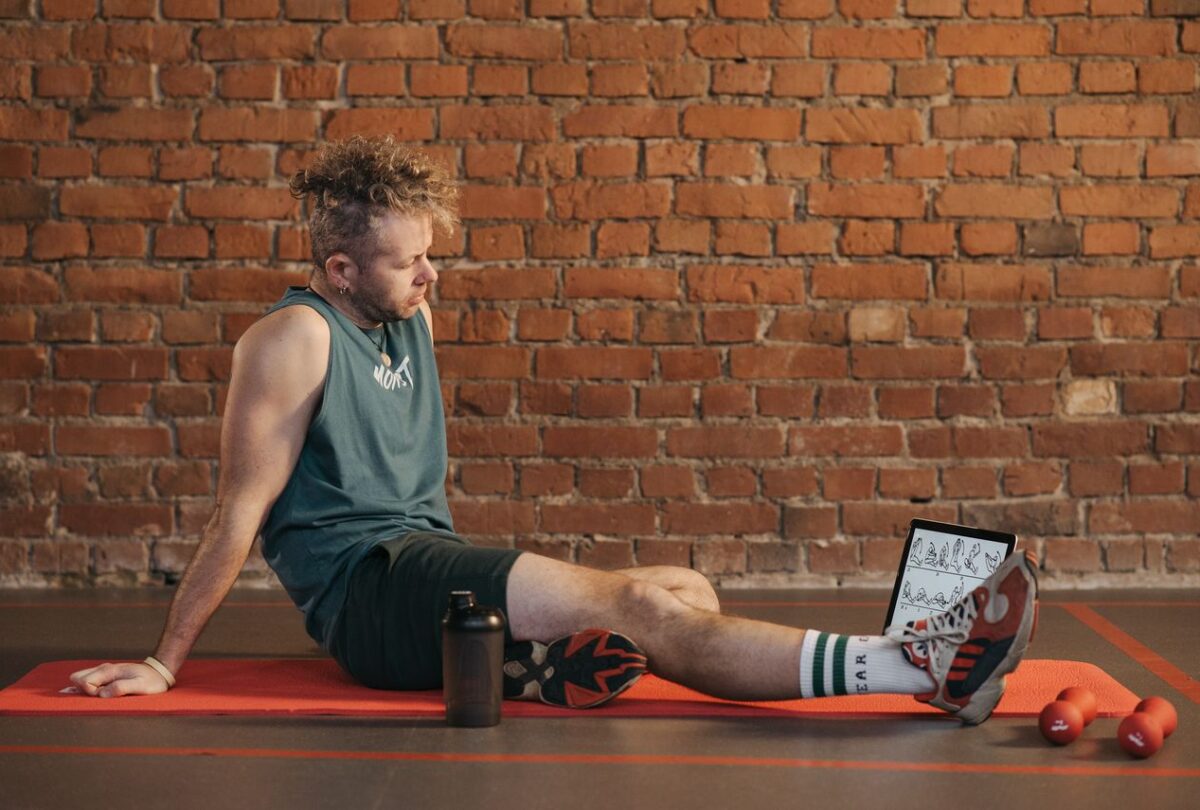 Man resting on an exercise mat beside dumbbells and a water bottle.