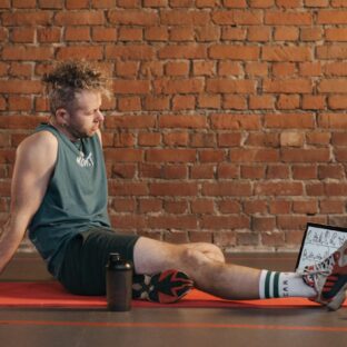Man resting on an exercise mat beside dumbbells and a water bottle.