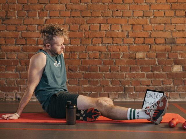 Man resting on an exercise mat beside dumbbells and a water bottle.