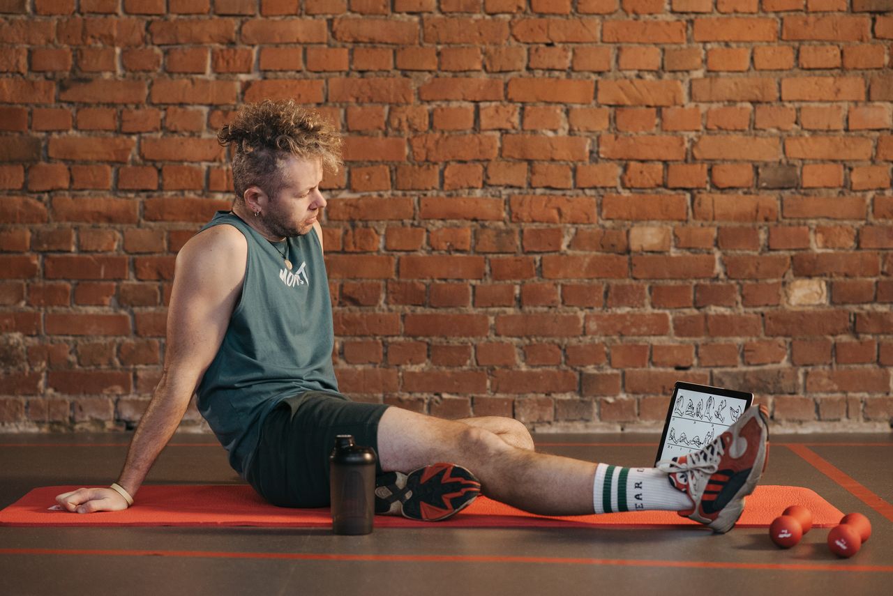Man resting on an exercise mat beside dumbbells and a water bottle.