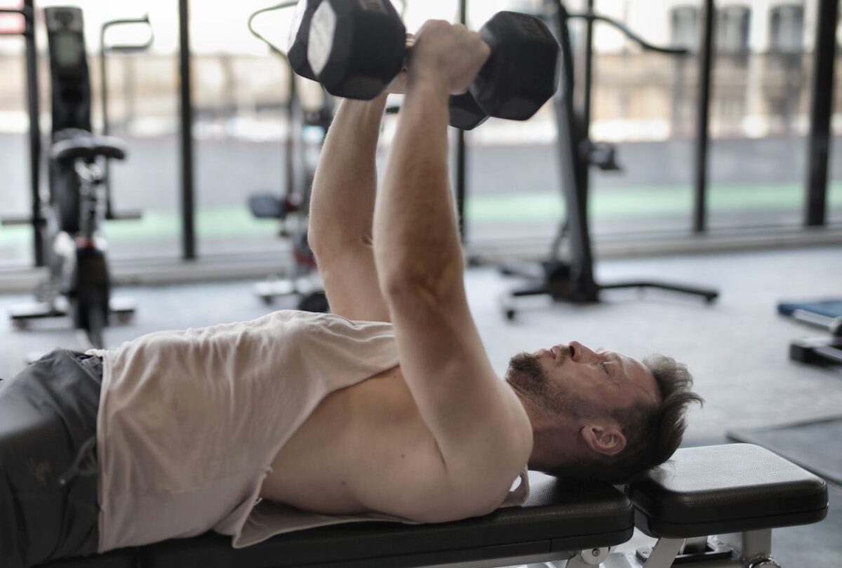 Man performing a dumbbell bench press in a gym.