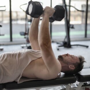 Man performing a dumbbell bench press in a gym.