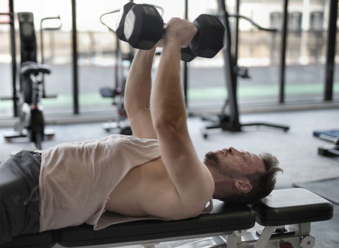 Man performing a dumbbell bench press in a gym.