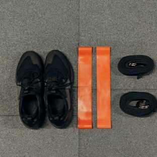 Black sneakers and orange resistance bands arranged on a gray floor.