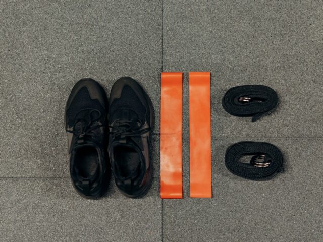 Black sneakers and orange resistance bands arranged on a gray floor.