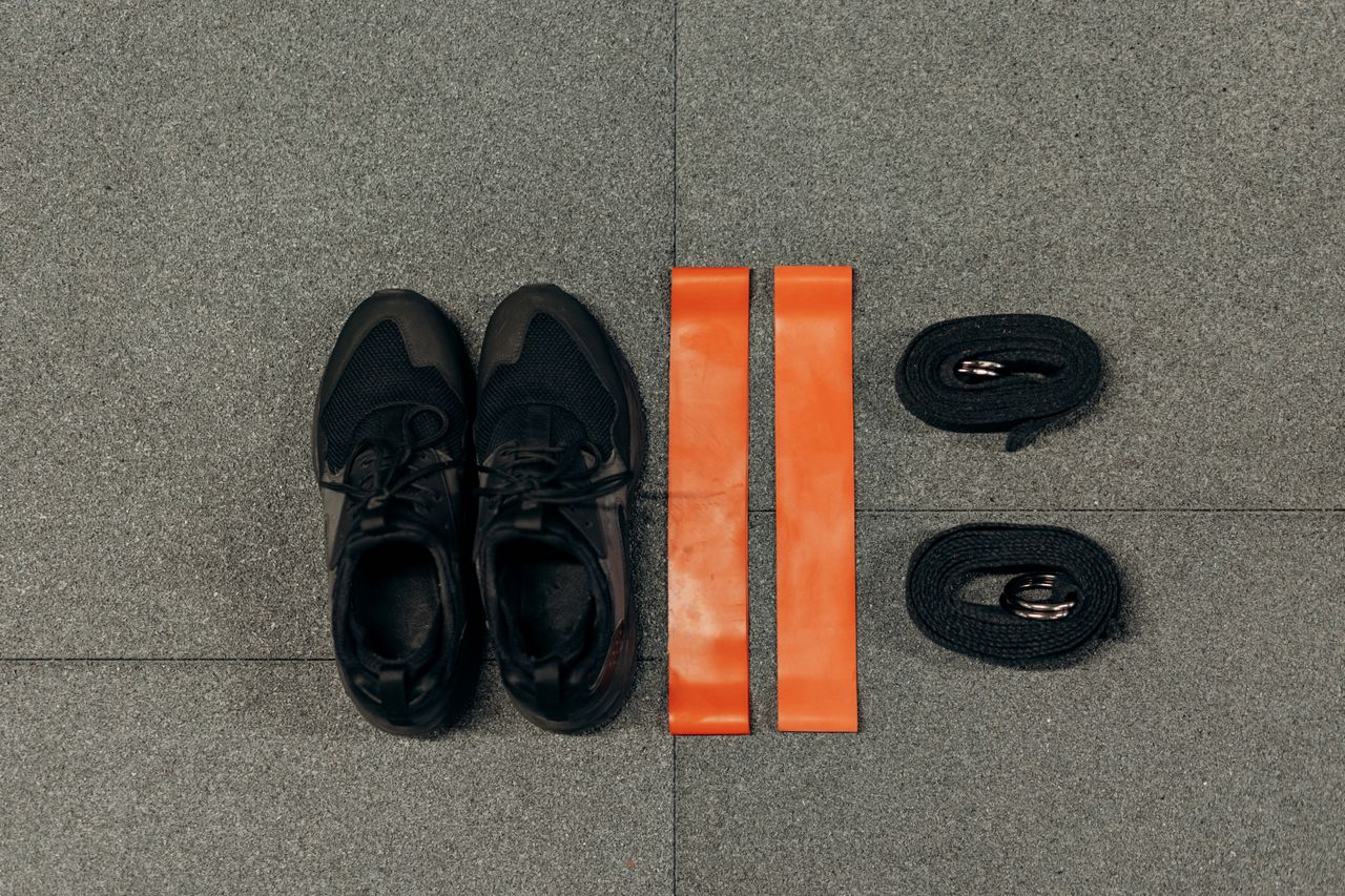 Black sneakers and orange resistance bands arranged on a gray floor.