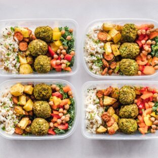 Four meal-prep containers filled with rice, falafel, chickpeas, and vegetables.