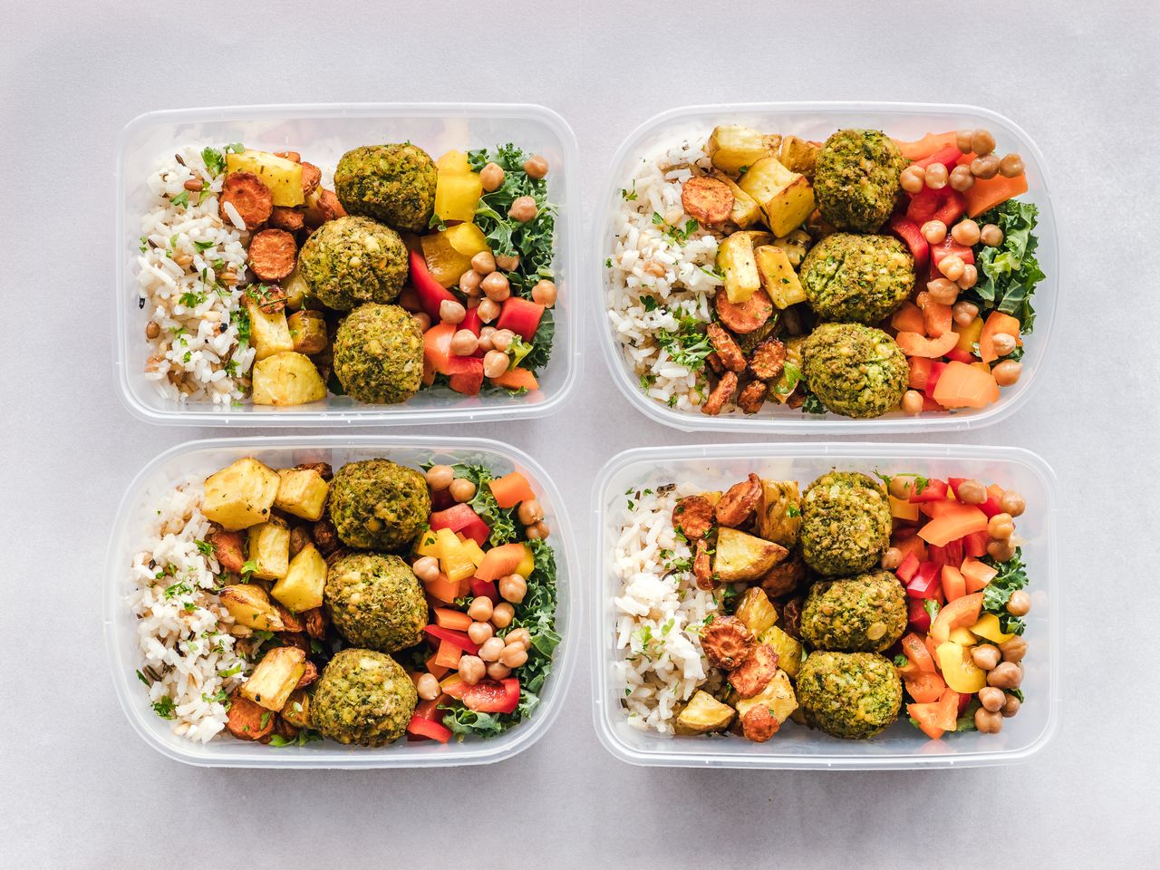 Four meal-prep containers filled with rice, falafel, chickpeas, and vegetables.