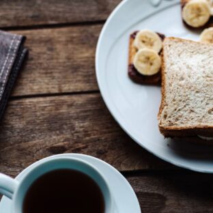 Bread and banana toast on a white plate beside a hot drink.