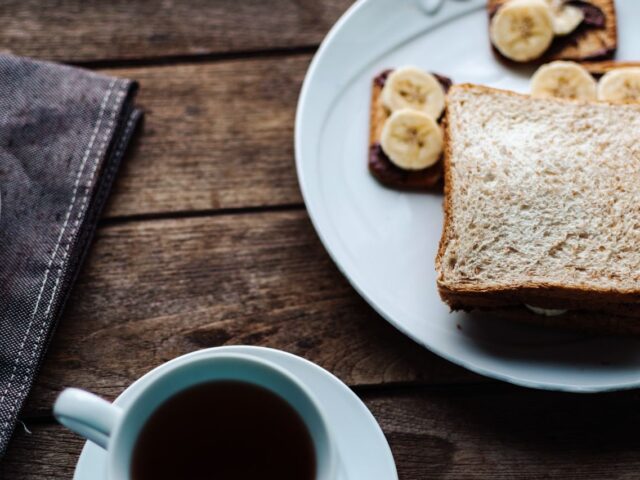 Bread and banana toast on a white plate beside a hot drink.