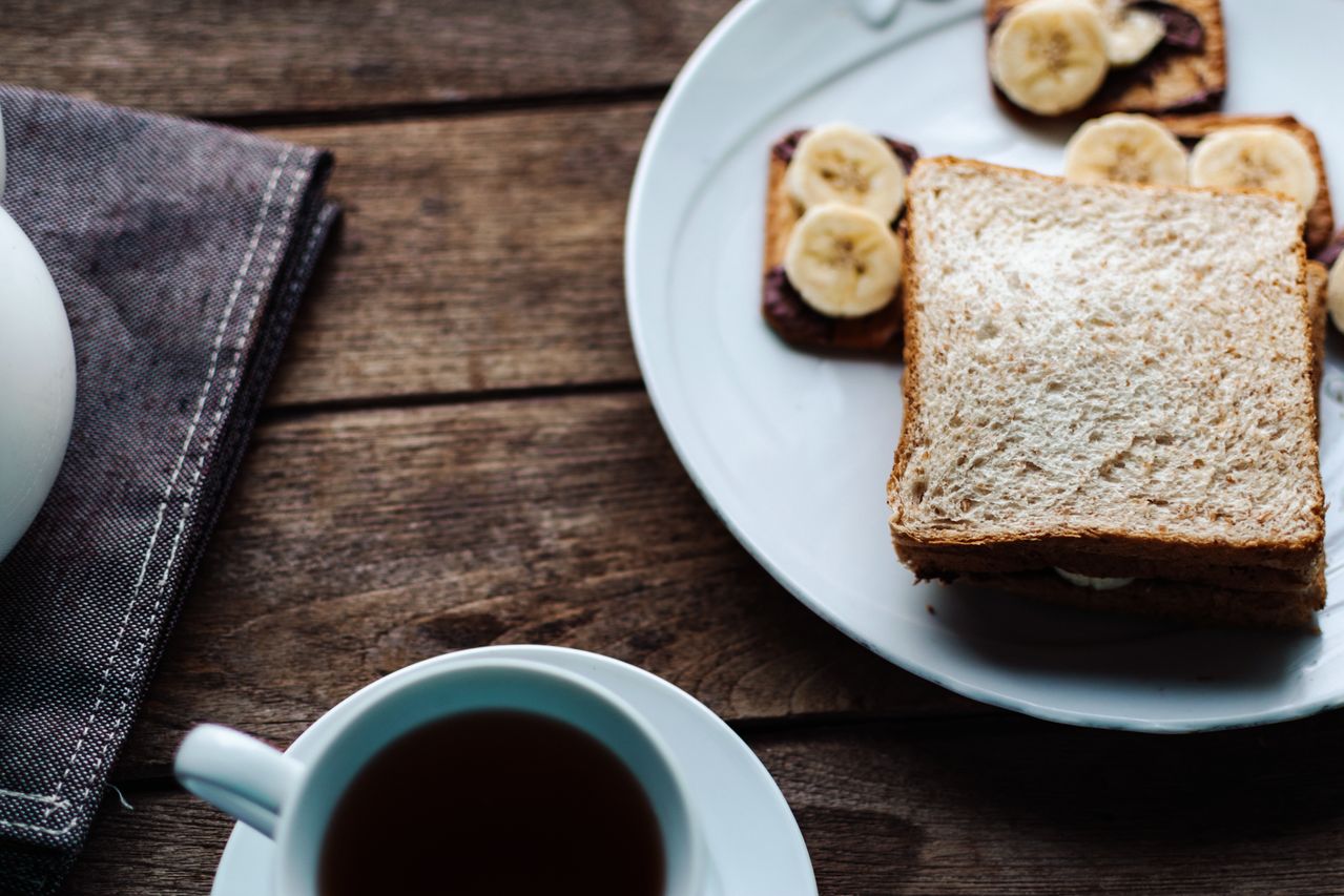 Bread and banana toast on a white plate beside a hot drink.