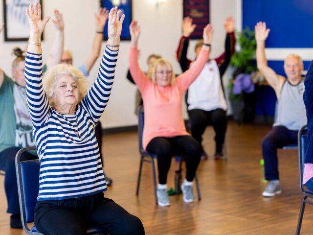 Older adults raising their arms during a seated exercise class.