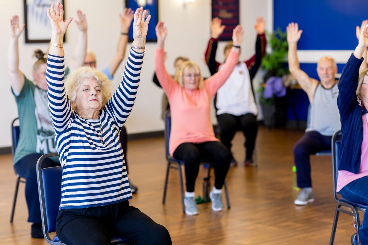 Older adults raising their arms during a seated exercise class.