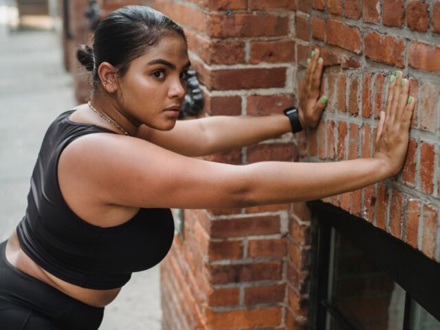 Woman leaning toward a brick wall with her hands planted for a wall push-up.