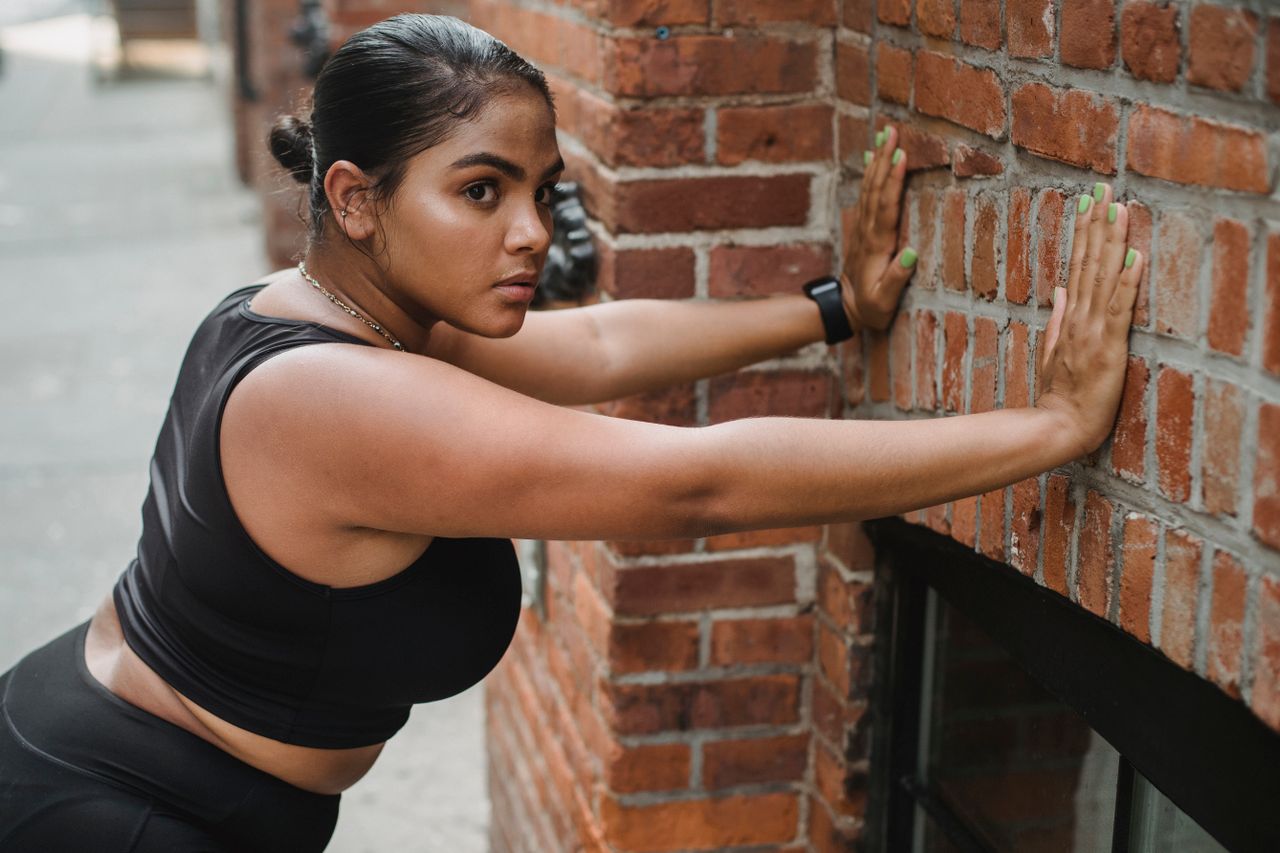 Woman leaning toward a brick wall with her hands planted for a wall push-up.