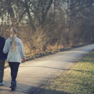 Two women walking along an outdoor path, viewed from behind.