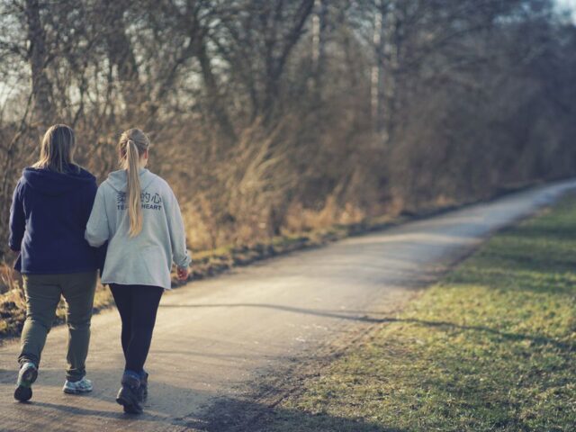 Two women walking along an outdoor path, viewed from behind.