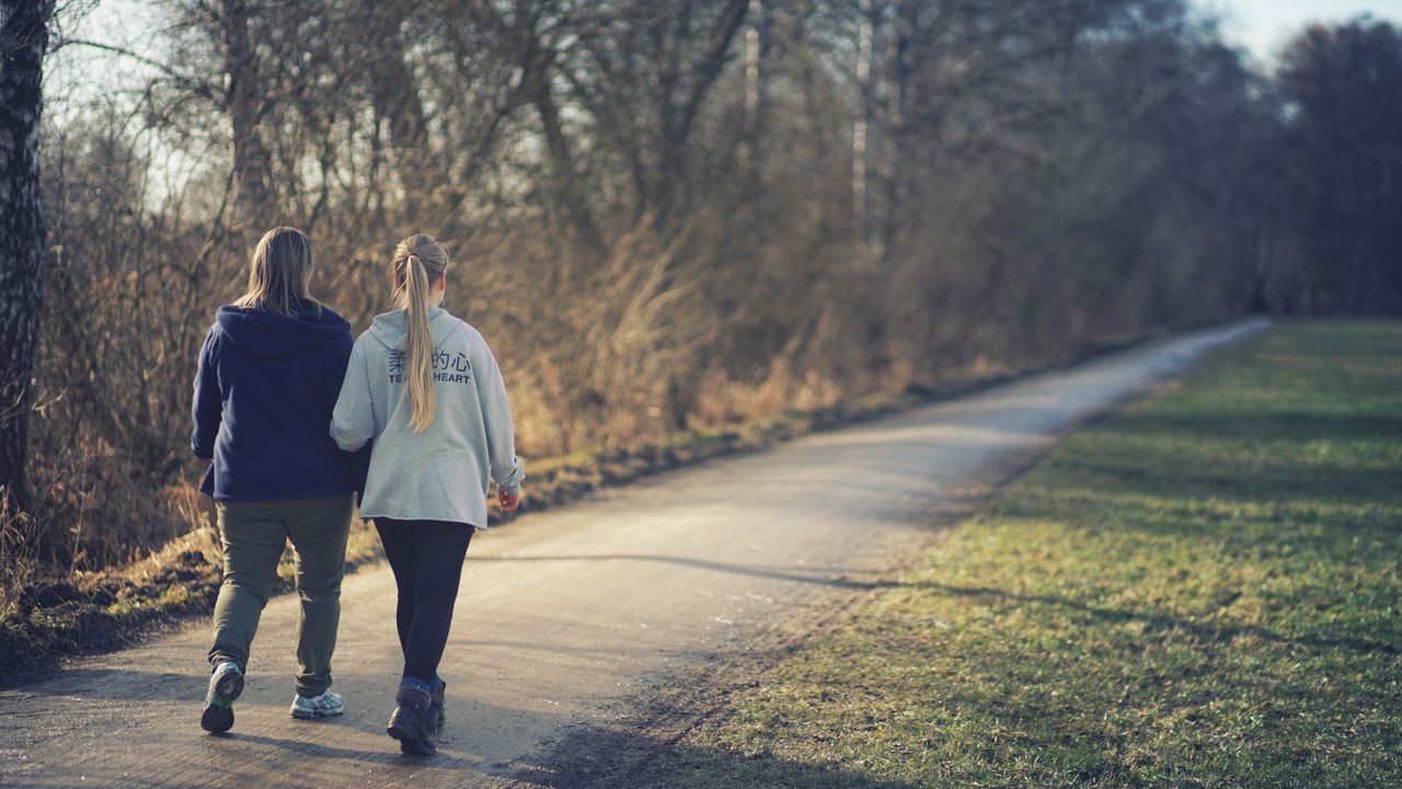 Two women walking along an outdoor path, viewed from behind.