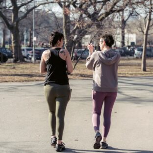 Two women in activewear walking together along a park path.