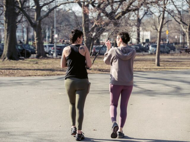 Two women in activewear walking together along a park path.