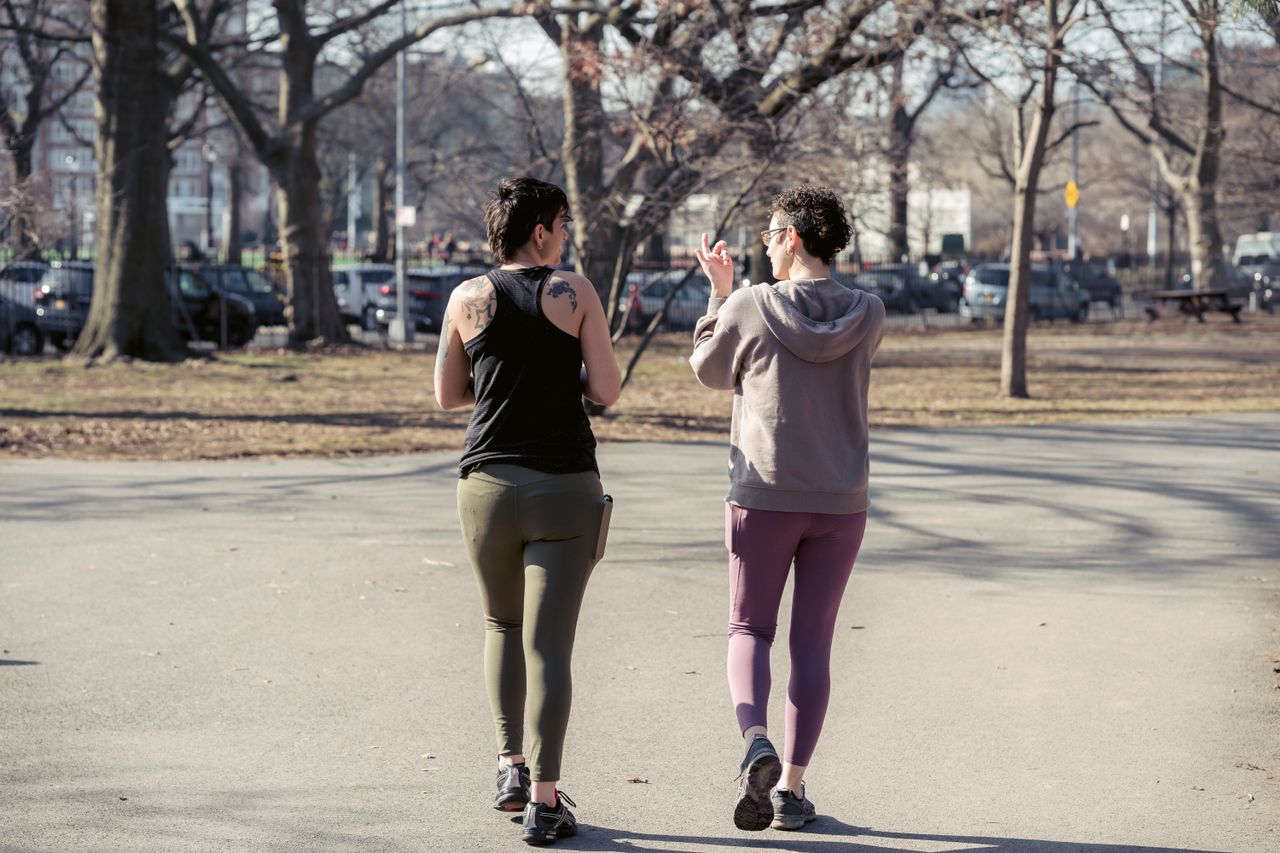 Two women in activewear walking together along a park path.