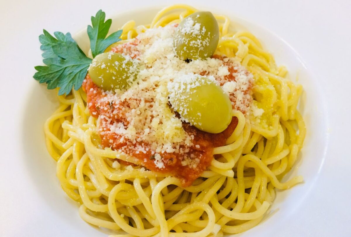 Spaghetti with tomato sauce, olives, grated cheese, and parsley on a white plate.