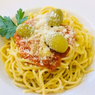 Spaghetti with tomato sauce, olives, grated cheese, and parsley on a white plate.