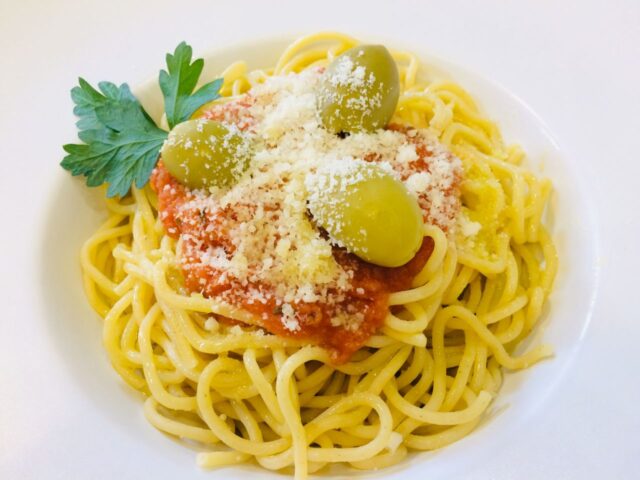 Spaghetti with tomato sauce, olives, grated cheese, and parsley on a white plate.