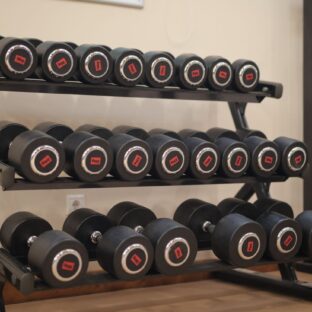 Pairs of dumbbells with different weight labels arranged on a three-tier gym rack.