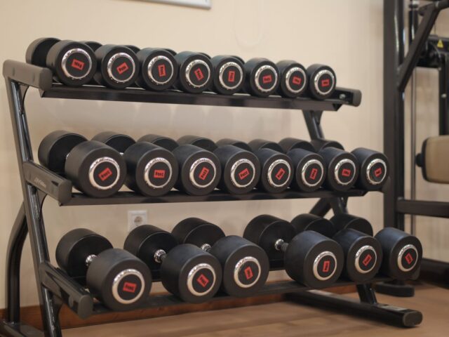 Pairs of dumbbells with different weight labels arranged on a three-tier gym rack.