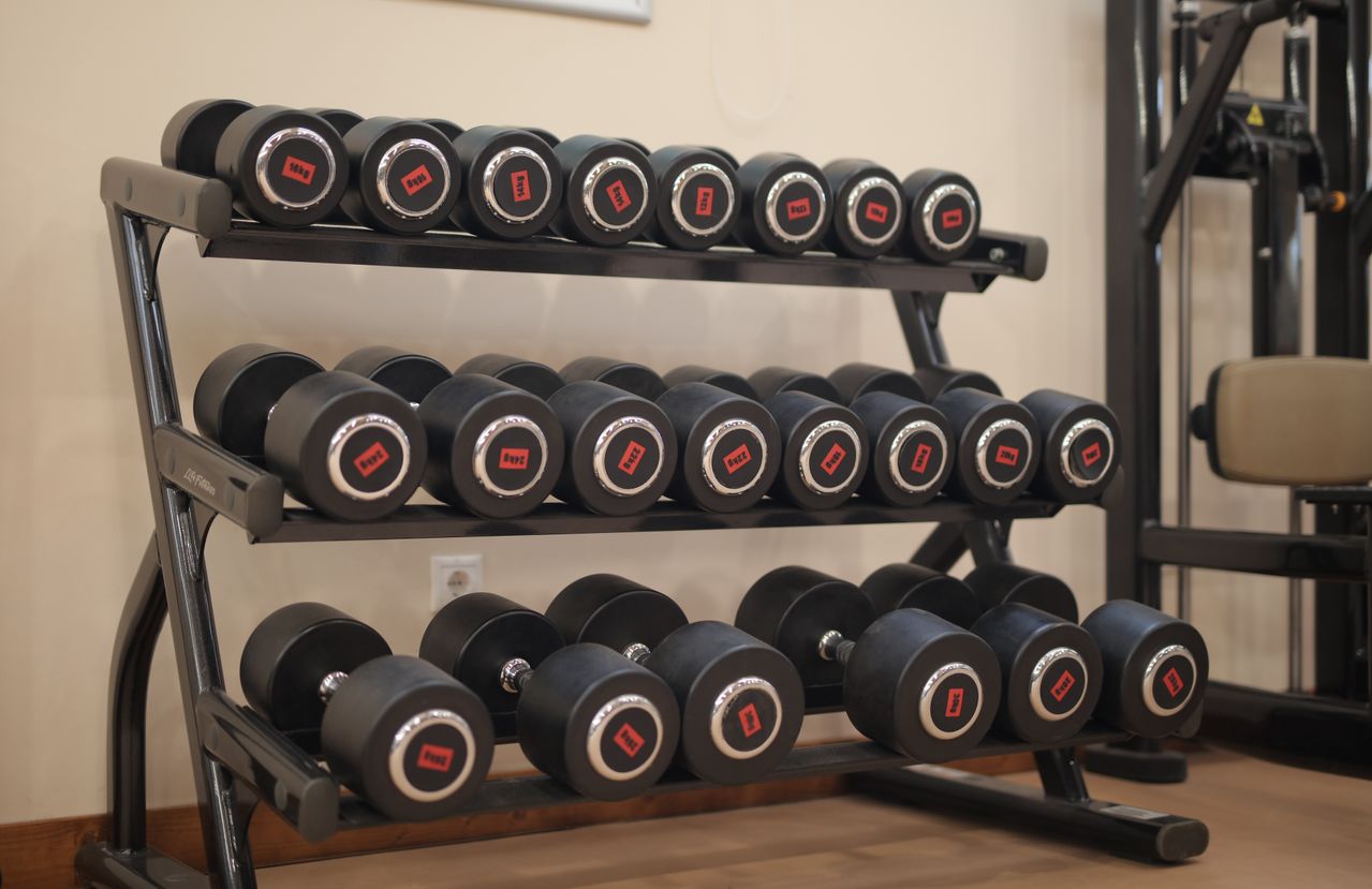 Pairs of dumbbells with different weight labels arranged on a three-tier gym rack.