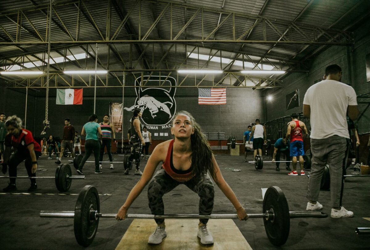 Woman setting up at a loaded barbell while other athletes train in a CrossFit gym.