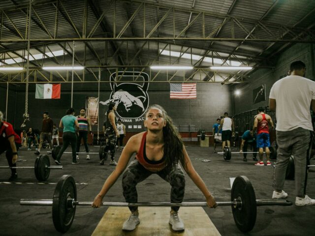 Woman setting up at a loaded barbell while other athletes train in a CrossFit gym.