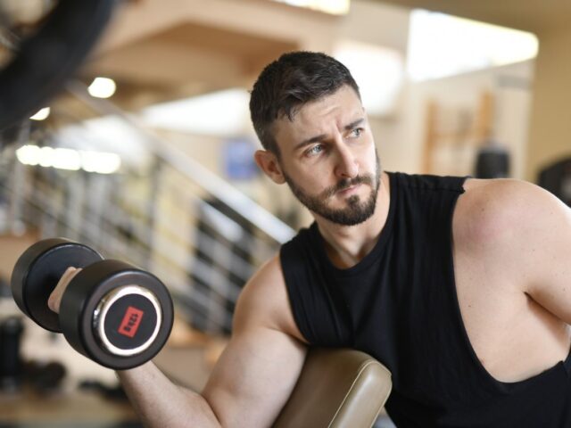 Man performing a dumbbell curl with his upper arm supported on a preacher bench