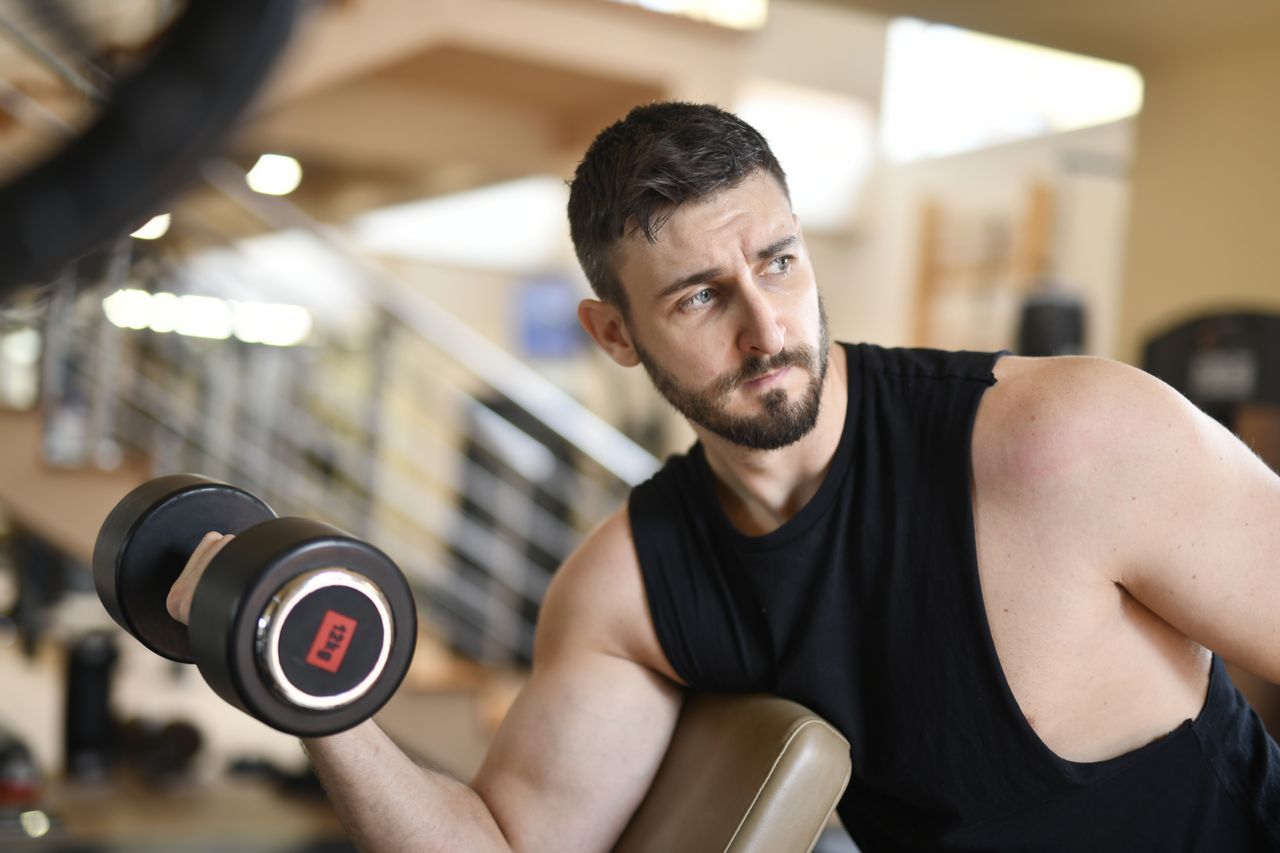 Man performing a dumbbell curl with his upper arm supported on a preacher bench