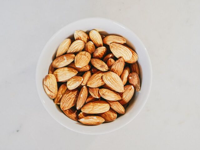 Whole almonds in a white bowl on a pale surface, viewed from above.
