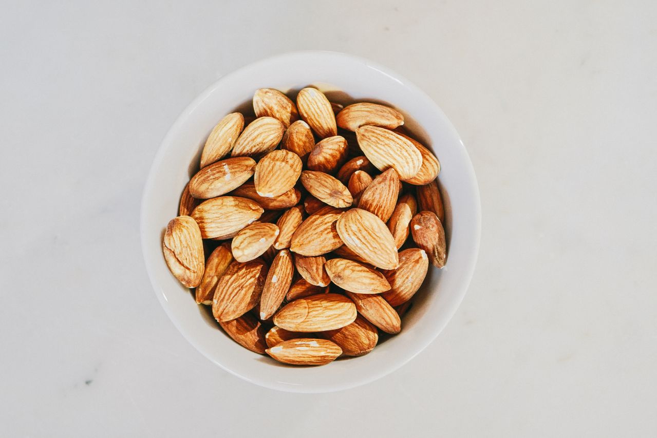 Whole almonds in a white bowl on a pale surface, viewed from above.