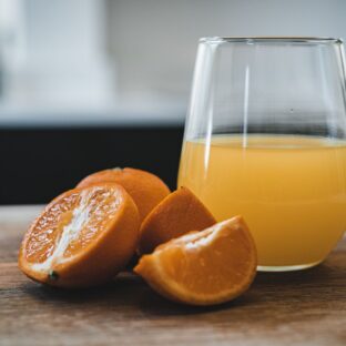 Glass of orange juice beside cut oranges on a wooden table.