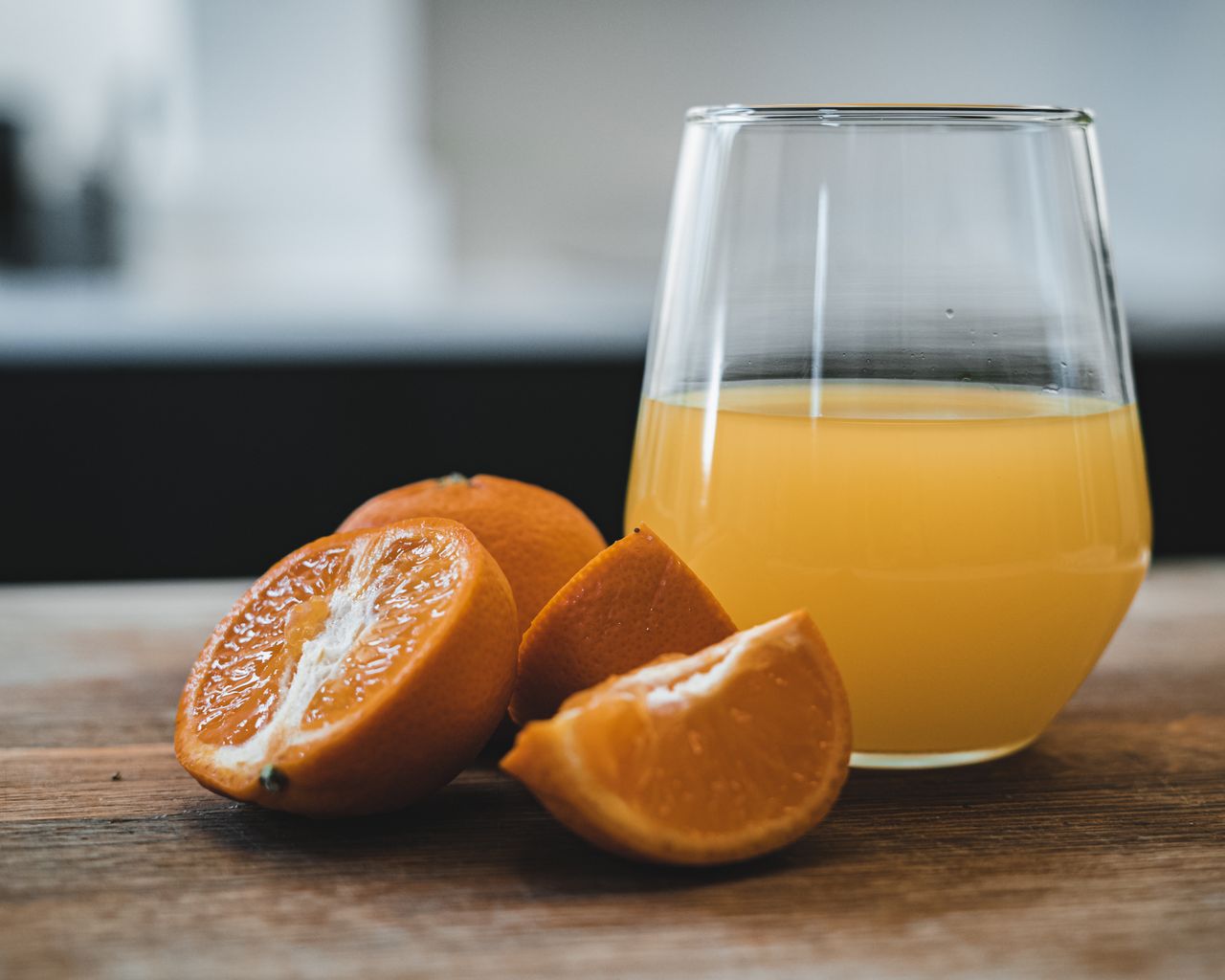 Glass of orange juice beside cut oranges on a wooden table.