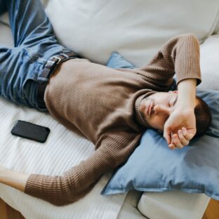 Man lying on a light-colored sofa with his eyes closed and head on a pillow.