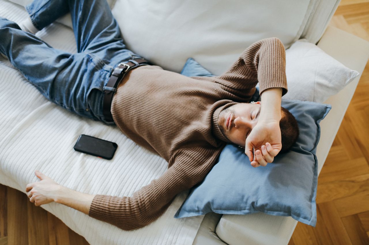 Man lying on a light-colored sofa with his eyes closed and head on a pillow.
