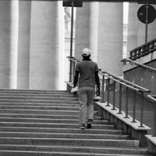 Black-and-white view of a person climbing a broad staircase with handrails.