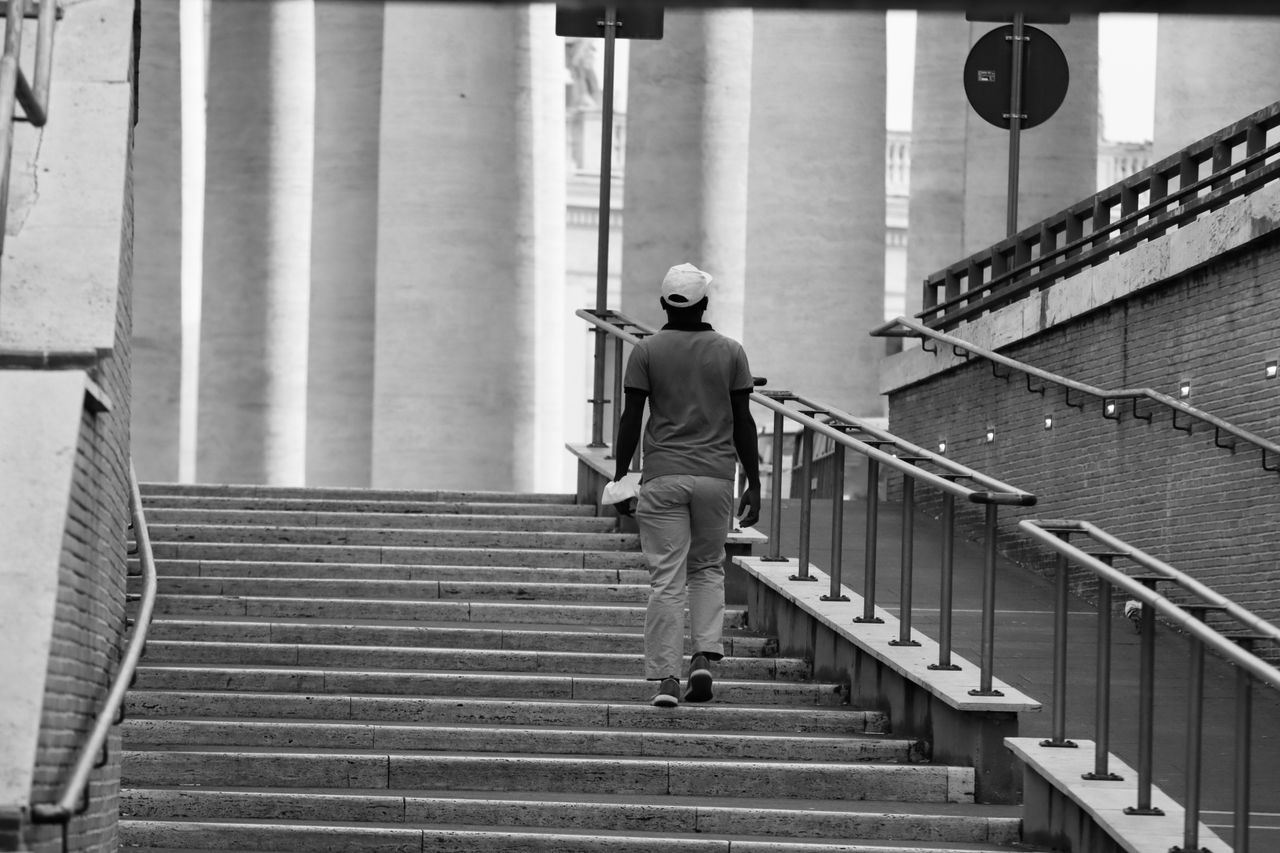 Black-and-white view of a person climbing a broad staircase with handrails.