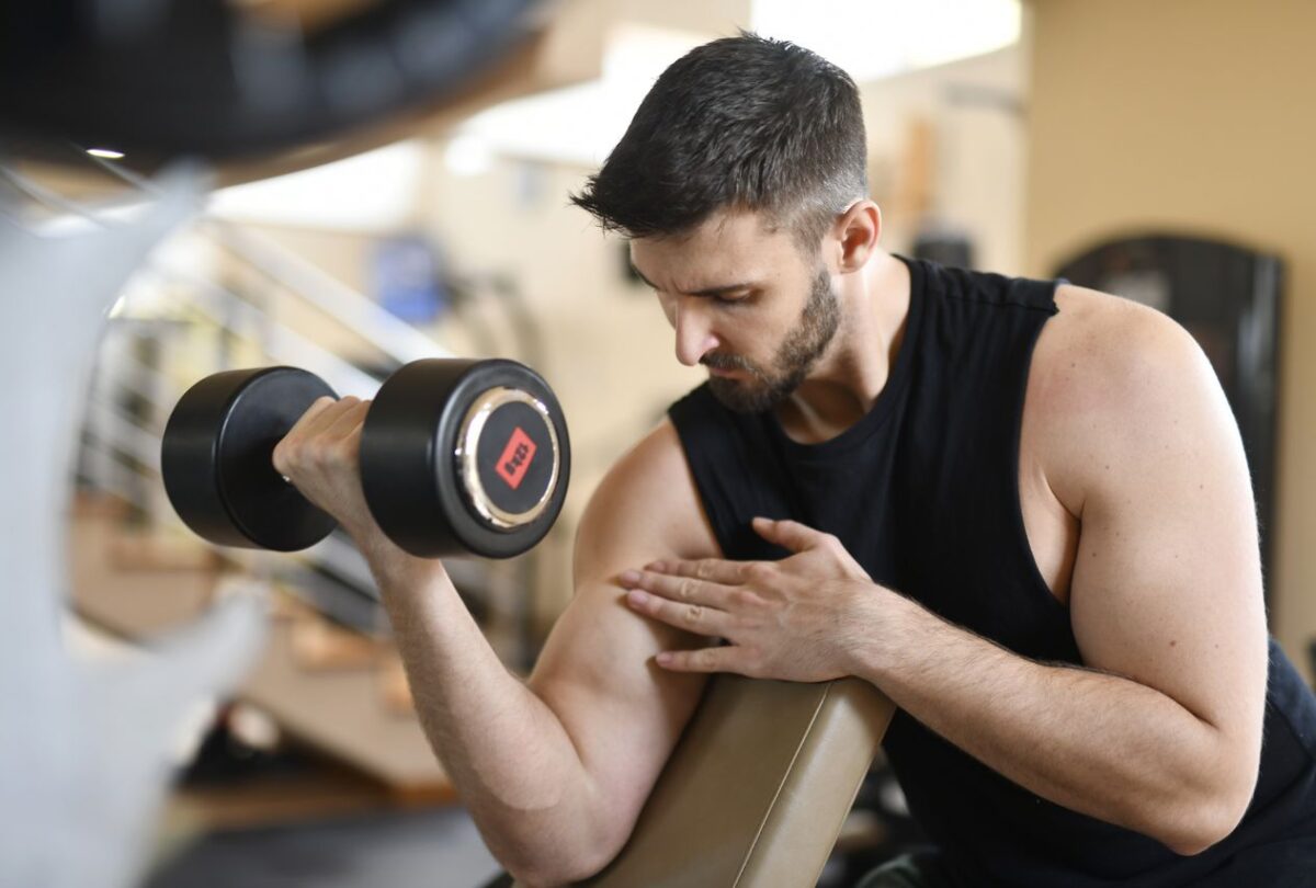 Man curling a dumbbell with his upper arm supported on a sloped preacher pad.