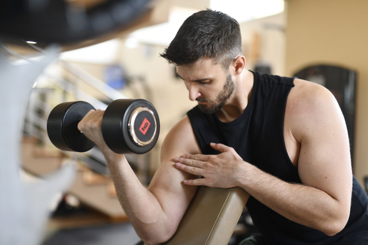 Man curling a dumbbell with his upper arm supported on a sloped preacher pad.